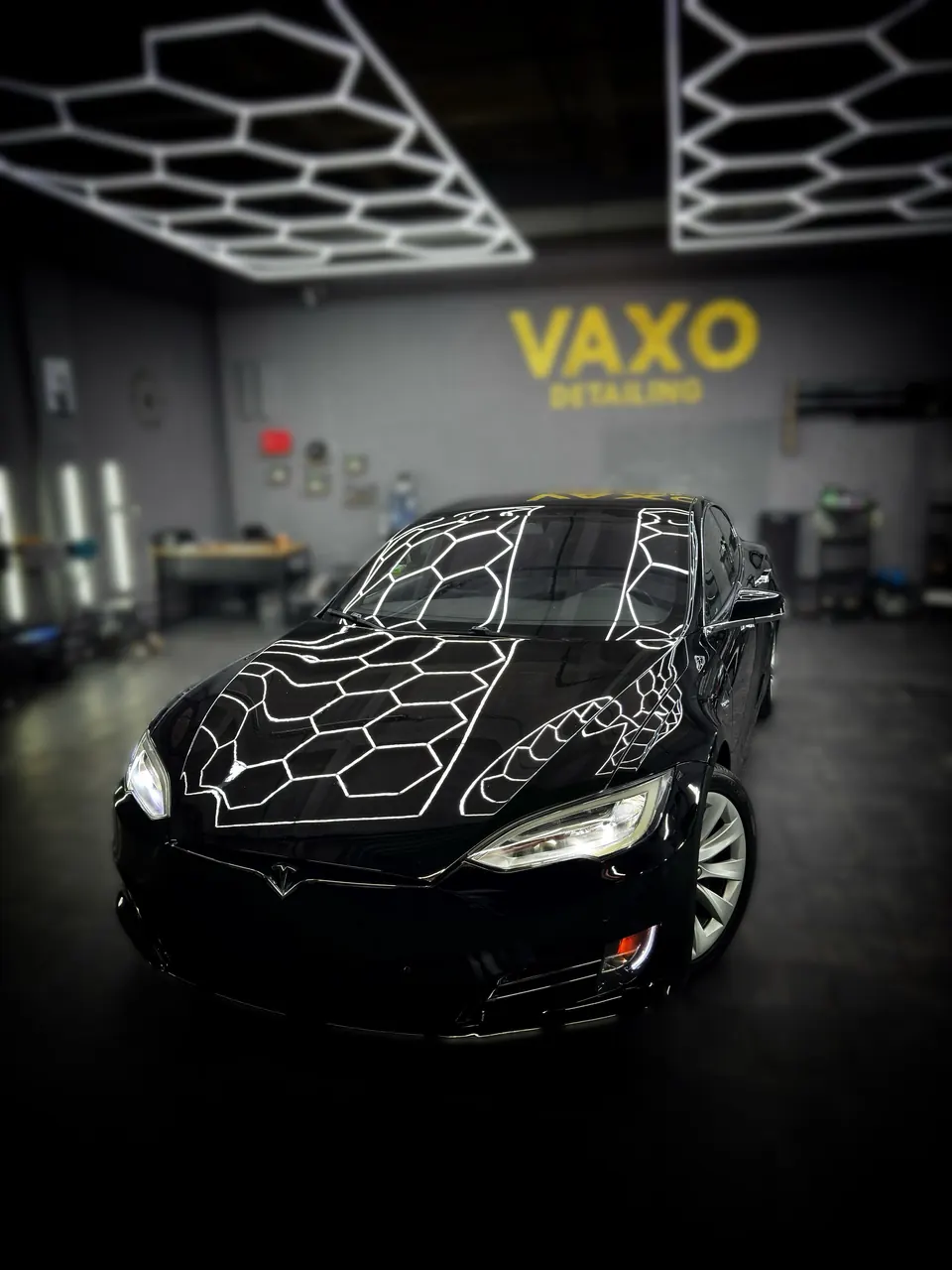 Чёрная Tesla Model S у стены VAXO, соты на капоте